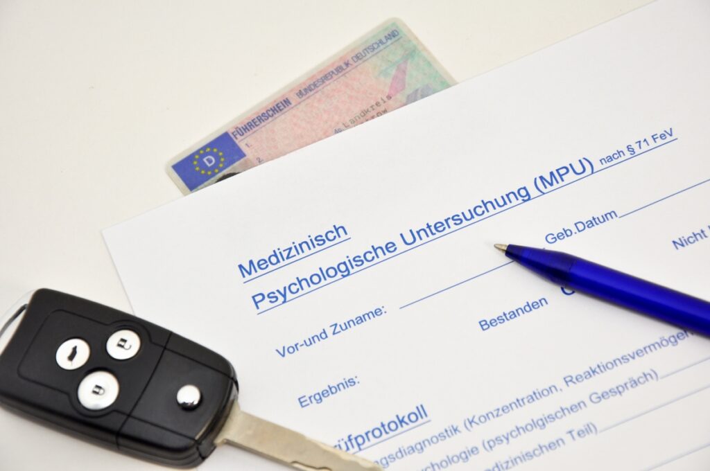 Ein Autoschlüssel, ein Führerschein und ein Fragebogen liegen auf einem weißen Tisch.