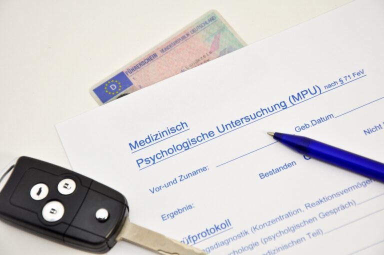Ein Autoschlüssel, ein Führerschein und ein Fragebogen liegen auf einem weißen Tisch.