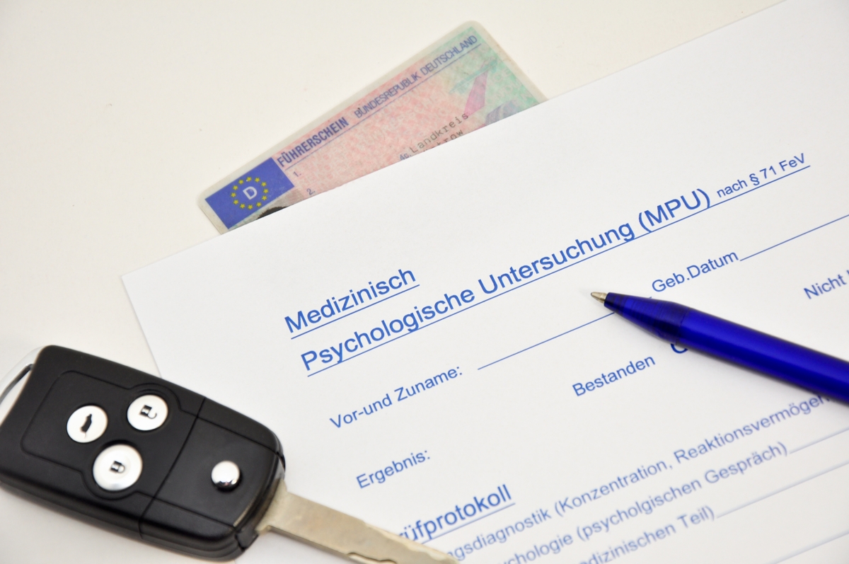 Ein Autoschlüssel, ein Führerschein und ein Fragebogen liegen auf einem weißen Tisch.